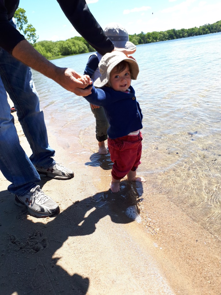 Florence standing in the surf, with her hands being held by her grandfather Mike.